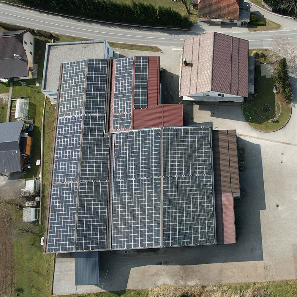 Zračni posnetek industrijske hale z večjimi polji sončnih panelov na strehi; okolišče z dvoriščem in objekti.