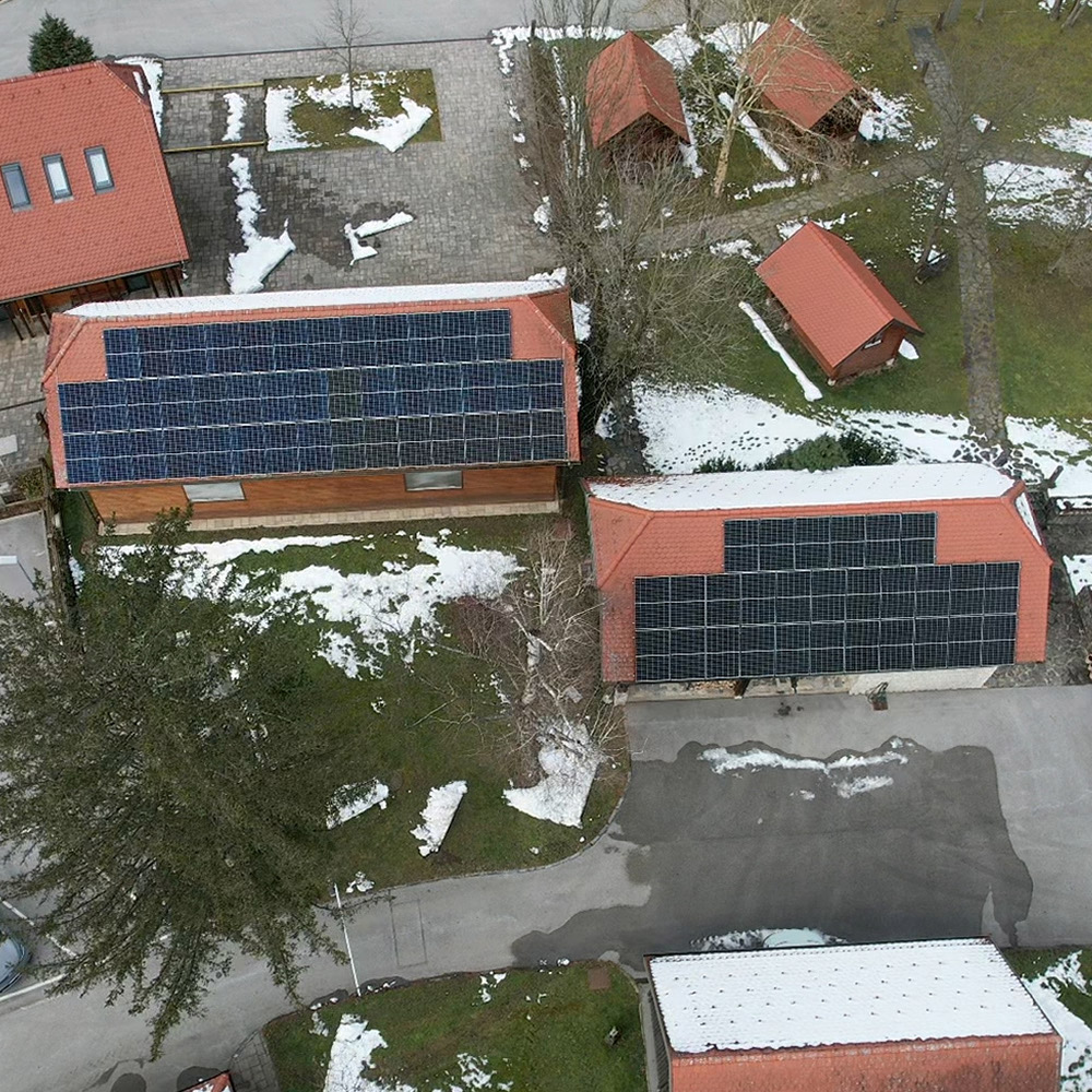 Zračni posnetek dveh objektov s sončnimi paneli na rdečih strešnih kritinah; okoli zelenica in zaplate snega (kamp).